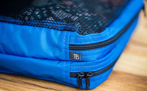 Each Small and Large Laundry Packing Cube has a small dark grey and white TB tab between the zipper and the sewn divider on the mesh side.